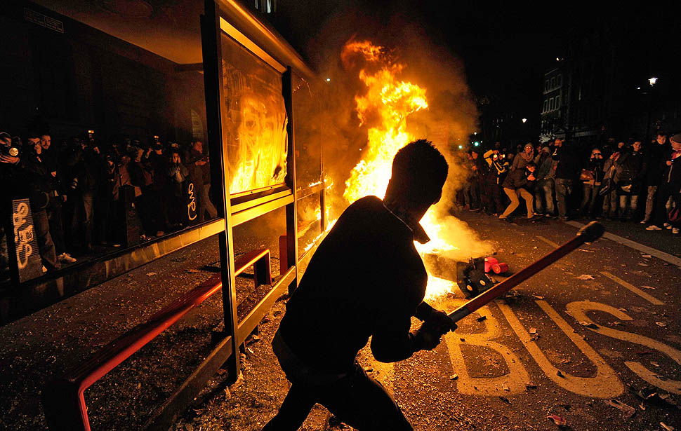 A demonstrator strikes a bus shelter near a fire made of plastic street furniture during a protest, in central London November 24, 2010. Demonstrators scuffled with police in central London on Wednesday when thousands of students and school pupils protested across Britain against government plans to raise university tuition fees.   REUTERS/Paul Hackett (BRITAIN - Tags: CIVIL UNREST POLITICS EDUCATION CRIME LAW)